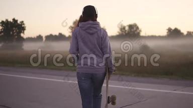 一个手拿滑板的时髦女孩的特写肖像。 那个红发女孩沿着废弃的公路走着